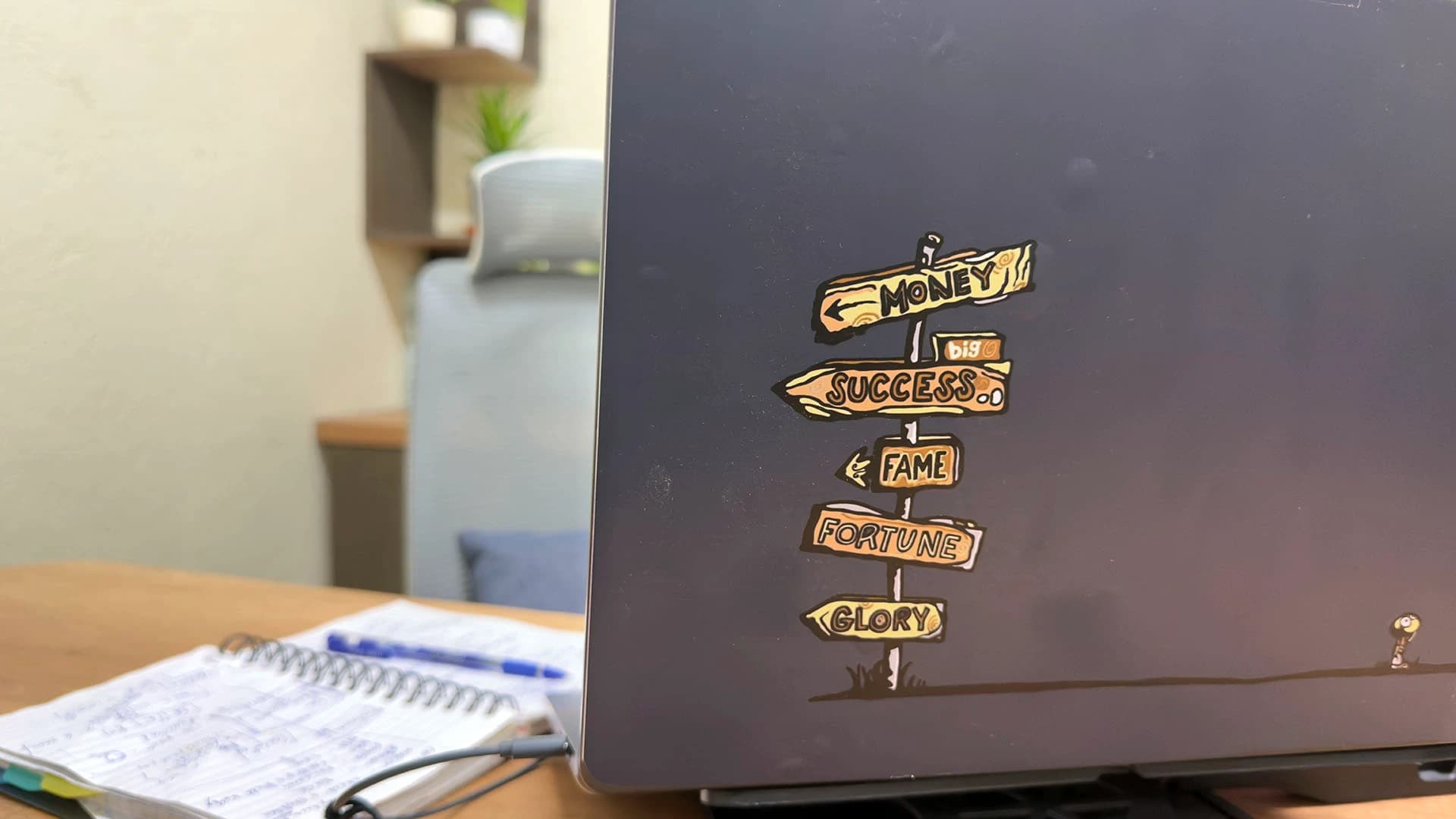 A closed laptop with a signpost sticker on its lid and an open notebook, Kolkata, India