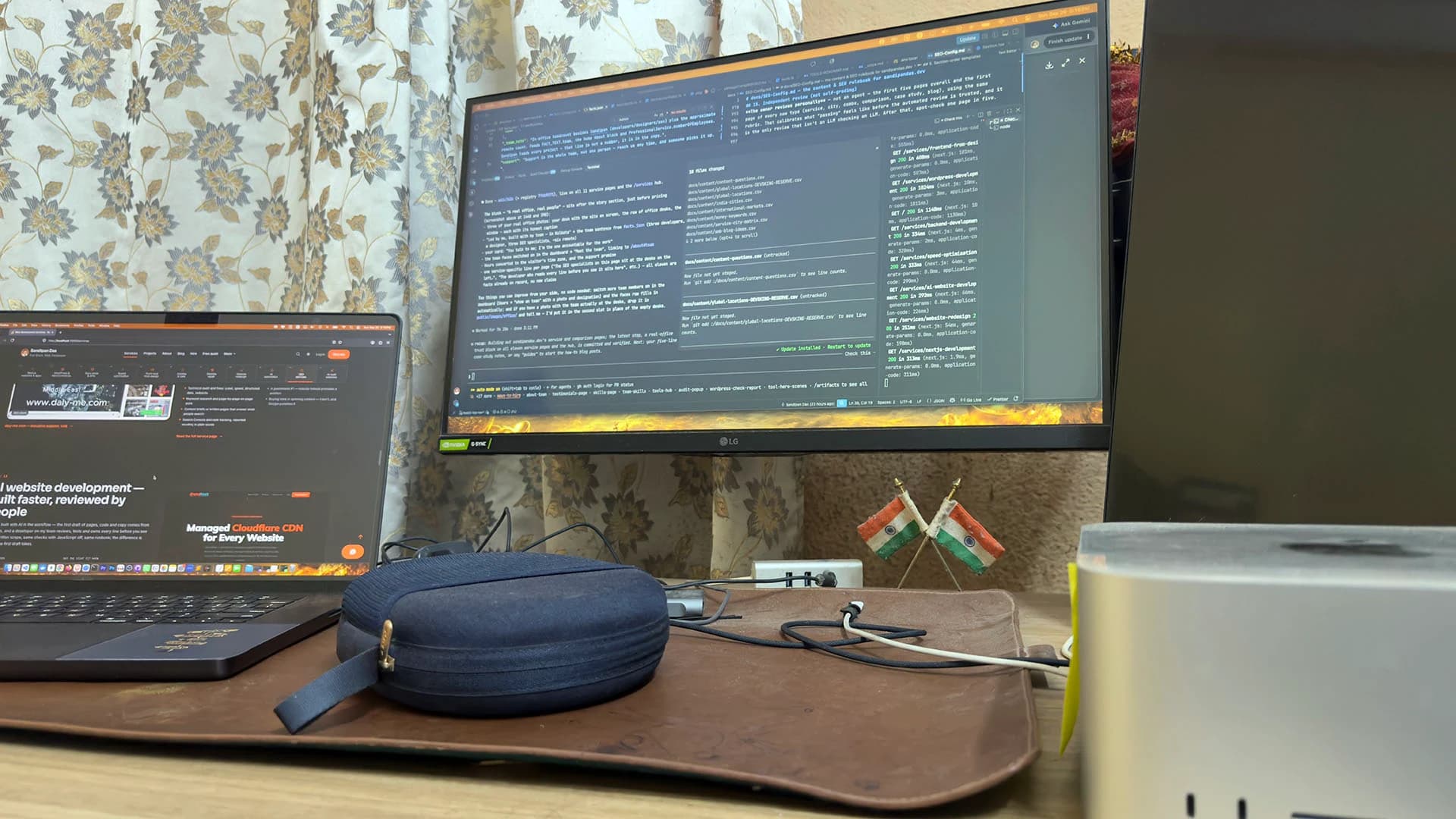 A monitor of code, a laptop to its left, a fabric pouch and two small Indian flags on a desk, Kolkata, India