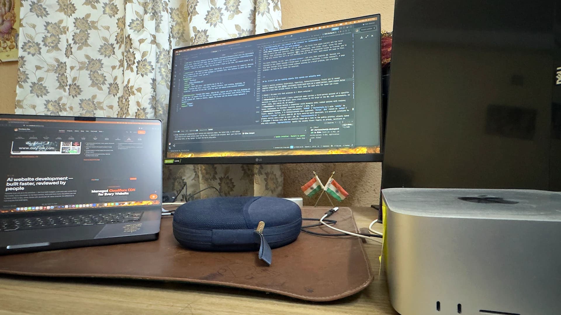 A laptop beside a widescreen monitor of code, a leather desk mat and a silver desktop computer, in Kolkata, India